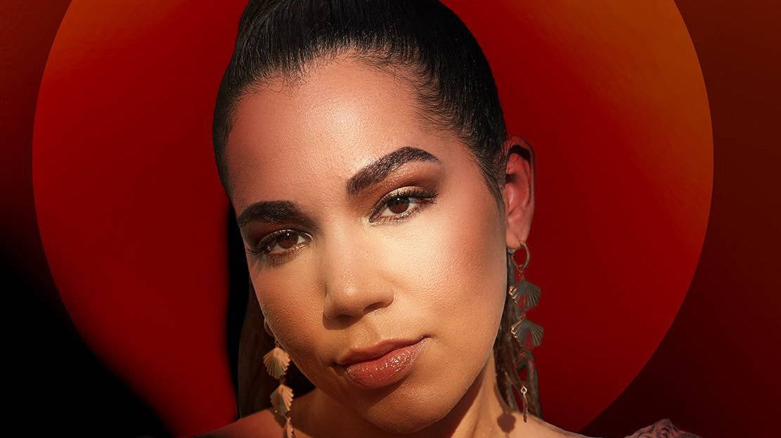 Portrait of a woman with dark hair and striking makeup against a red circular background.