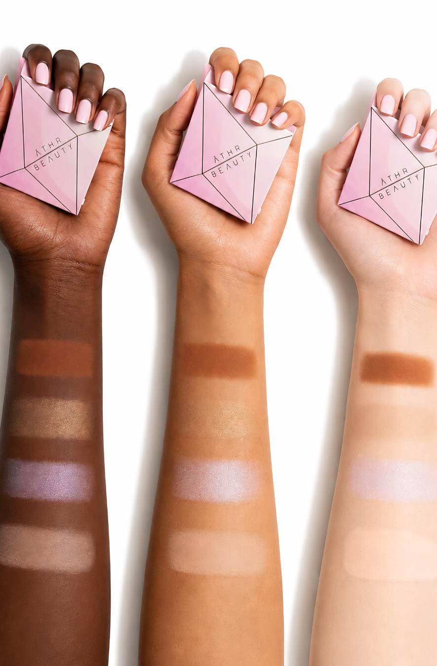 Three hands holding pink makeup products with color swatches on skin tones.