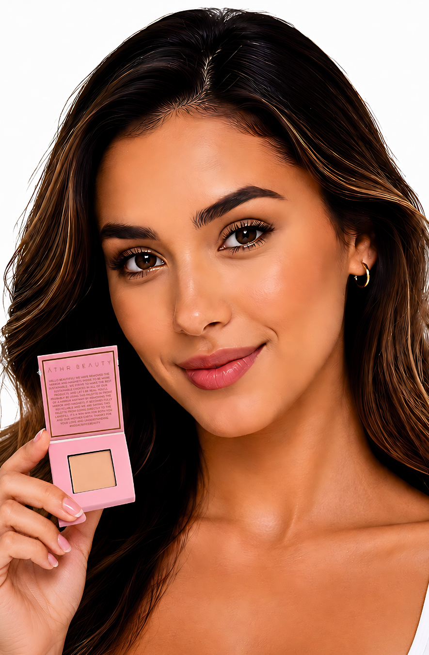 Model holding Athr Beauty's pink makeup compact of the 'Desert Mirage Blurring Powder' in the shade 'Citrine Sand' (a soft, warm beige with a banana-yellow tint) with a white background