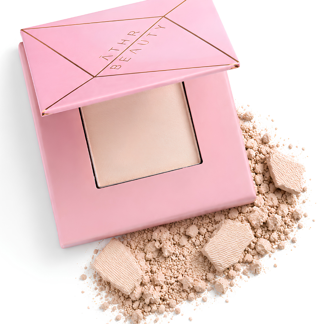Athr Beauty's pink makeup compact of the 'Desert Mirage Blurring Powder' with open lid and scattered powder in the shade 'Rose Mesa' (a soft, creamy beige with a subtle pink tint) on a white background