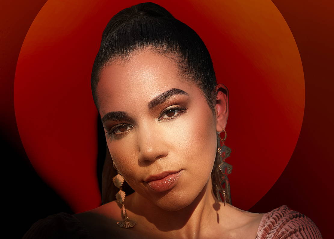 Portrait of a woman with dark hair and striking makeup against a red circular background.